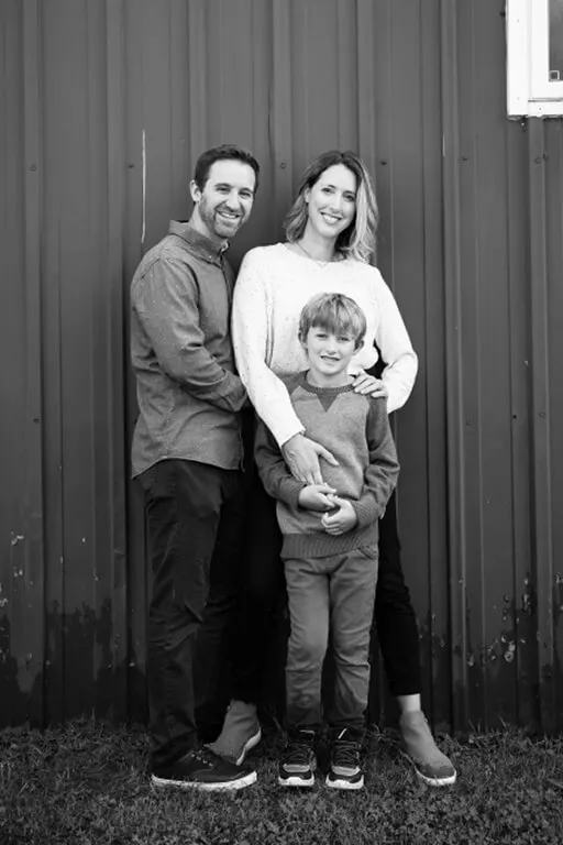 A family of three posting near a red wall.